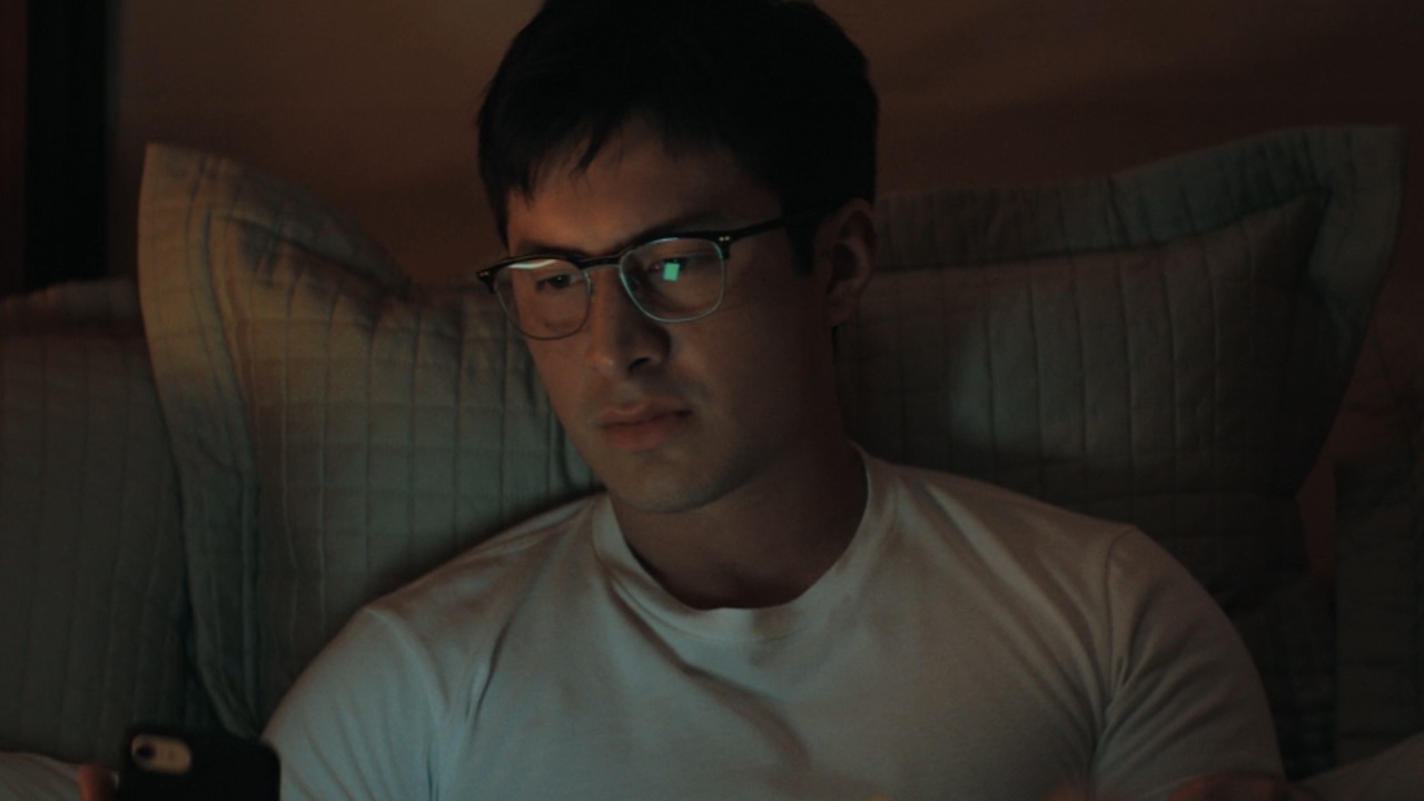 Hudson Williams wearing glasses on the phone in Heated Rivalry. 