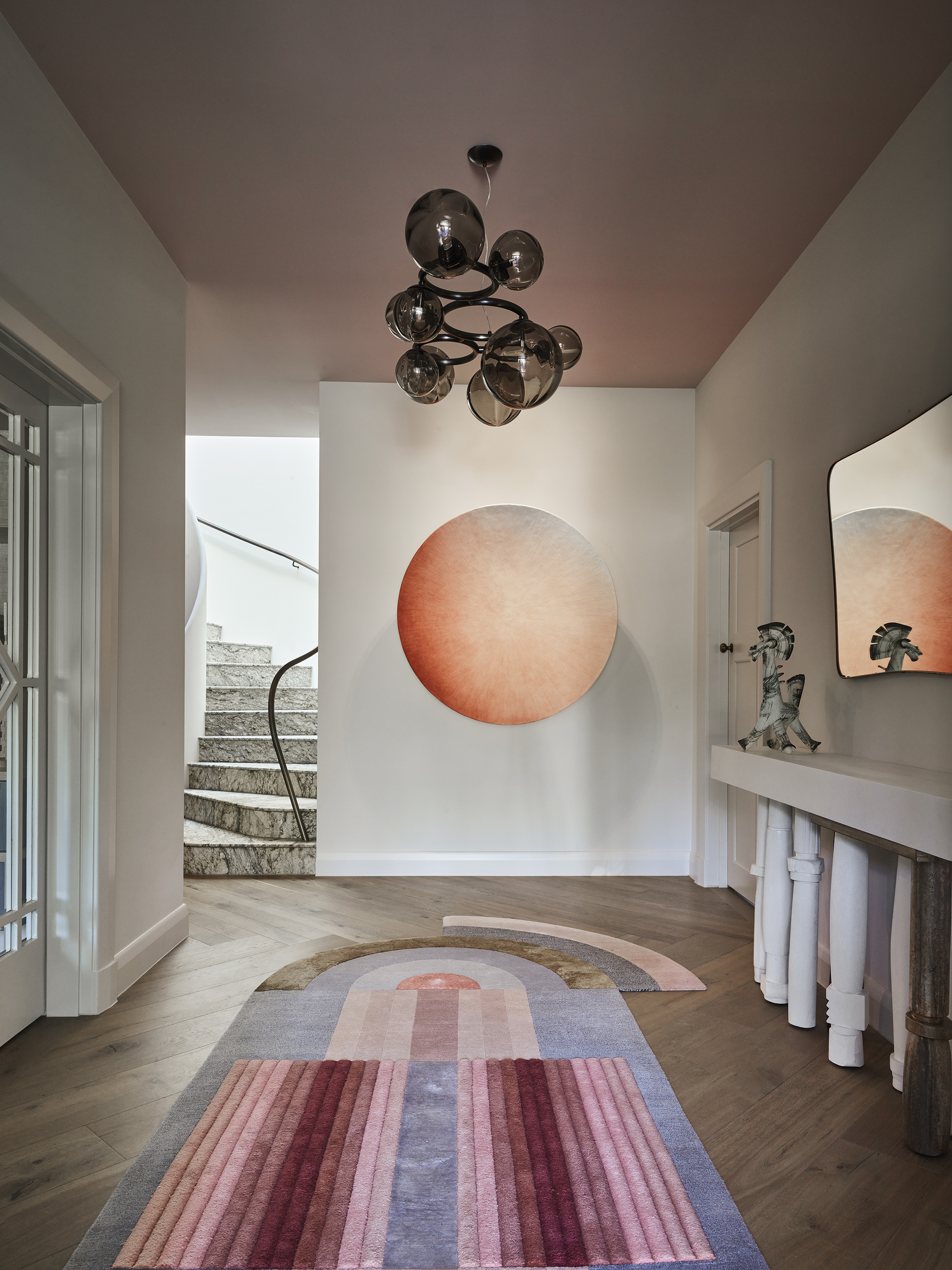 modern entryway with timber floors, pink colored ceiling, statement art, pendant light, colorful irregular rug and stone staircase