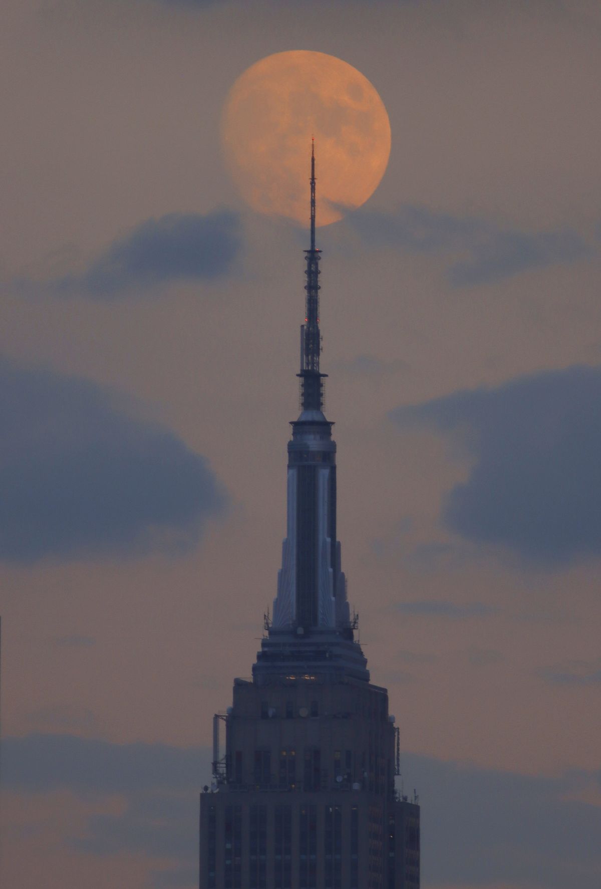 A 95 percent illuminated waxing gibbous moon rises behind the Empire State Building in New York City on October 7, 2022, as seen from Union City, New Jersey.