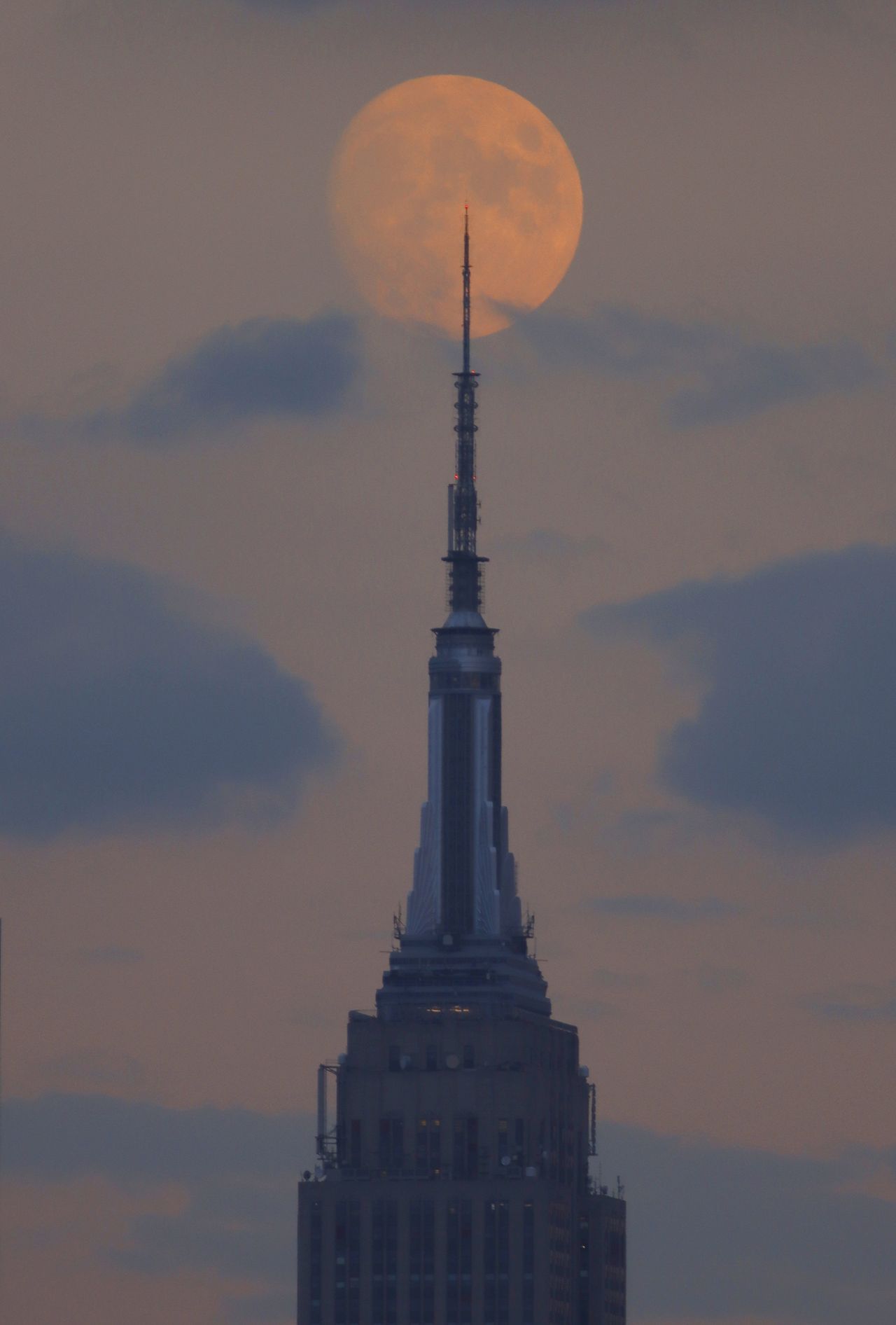 A 95 percent illuminated waxing gibbous moon rises behind the Empire State Building in New York City on October 7, 2022, as seen from Union City, New Jersey.