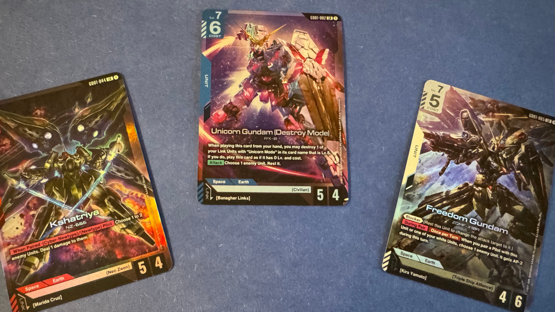 Three cards featuring Gundam mechs laid out on a blue velvet surface