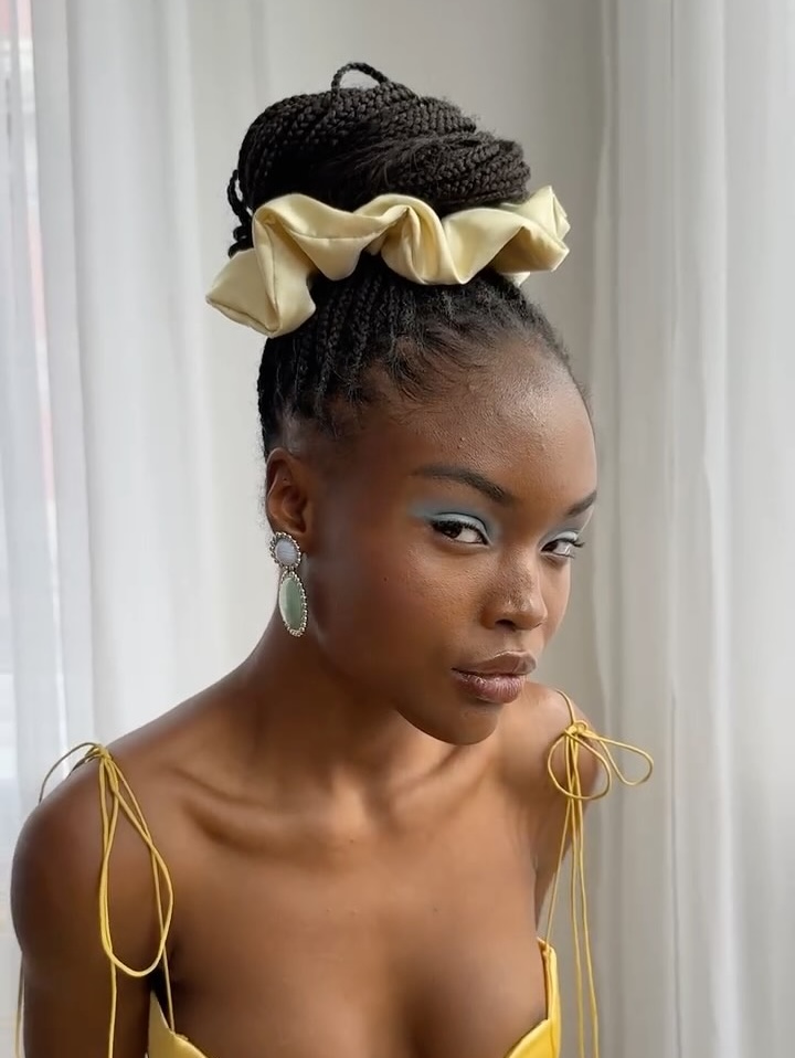 A model wears knotless braids in a top knot with a yellow, oversized Lelet NY scrunchie