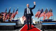 full-body shot of stephen miller waving in front of a bunch of american flags at an event