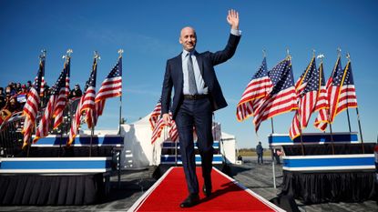 full-body shot of stephen miller waving in front of a bunch of american flags at an event