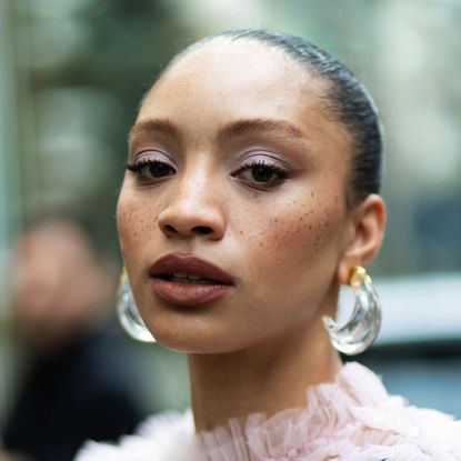 a woman with visible freckles wearing watercolour flush make-up and perspex earrings