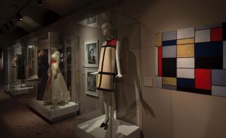 A room with dresses on display with the focus on the geometric design shift dress, next to the artist’s painting on the wall by which it was inspired