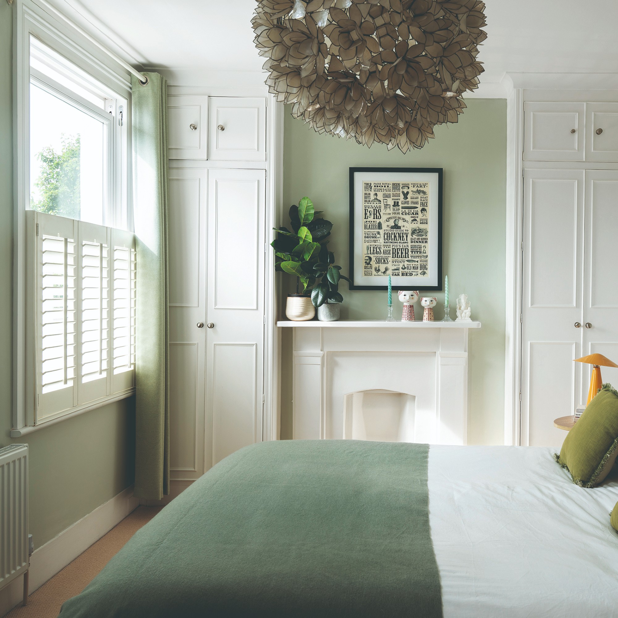 A sage green bedroom with white shutters and tonal sage green curtains on the window