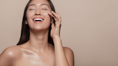 smiling woman with really glowy skin applying face cream - getty images 1142851205