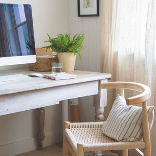 Office area with a wooden desk and woven wooden chair, a computer screen, and plant pots on the desk