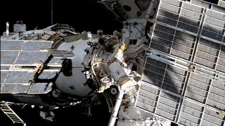 Two spacesuited cosmonauts are seen working outside a large space station set against the blackness of space.