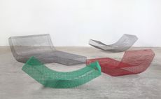4 modular sun lounge seats based on a grid structure, made of metallic net. two in grey, one in red and one in green. Photographed in a room with white walls and grey floor.