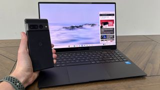 Samsung Galaxy Chromebook Plus on table with hand holding Pixel 7 Pro