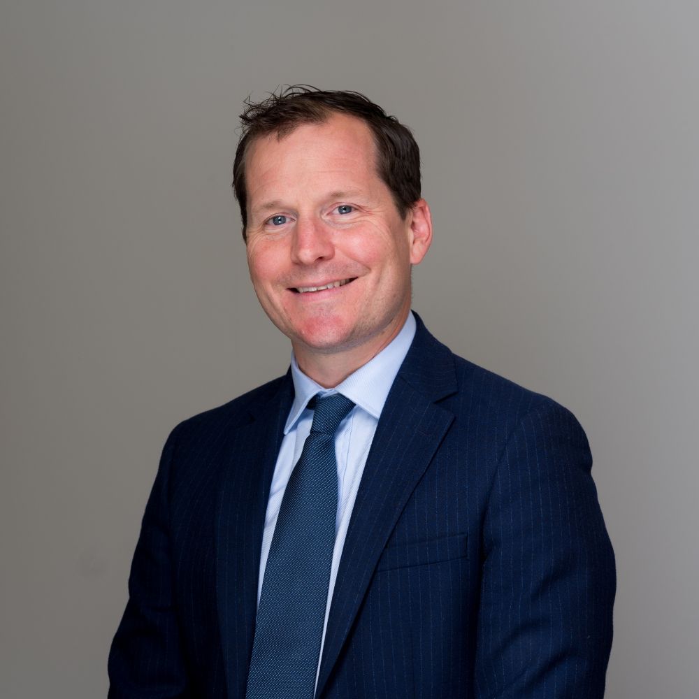 male with short dark hair wearing navy suit, blue shirt and blue tie