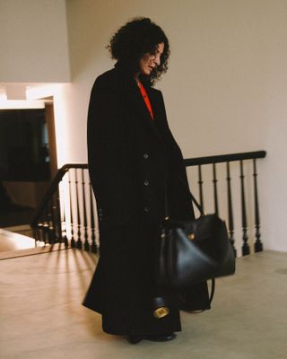 Neelam Ahooja in a black coat, red shirt, and black Balenciaga Rodeo bag.