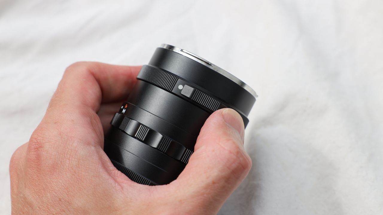Thypoch Simera 28mm f/1.4 lens held in a hand on a beige cloth
