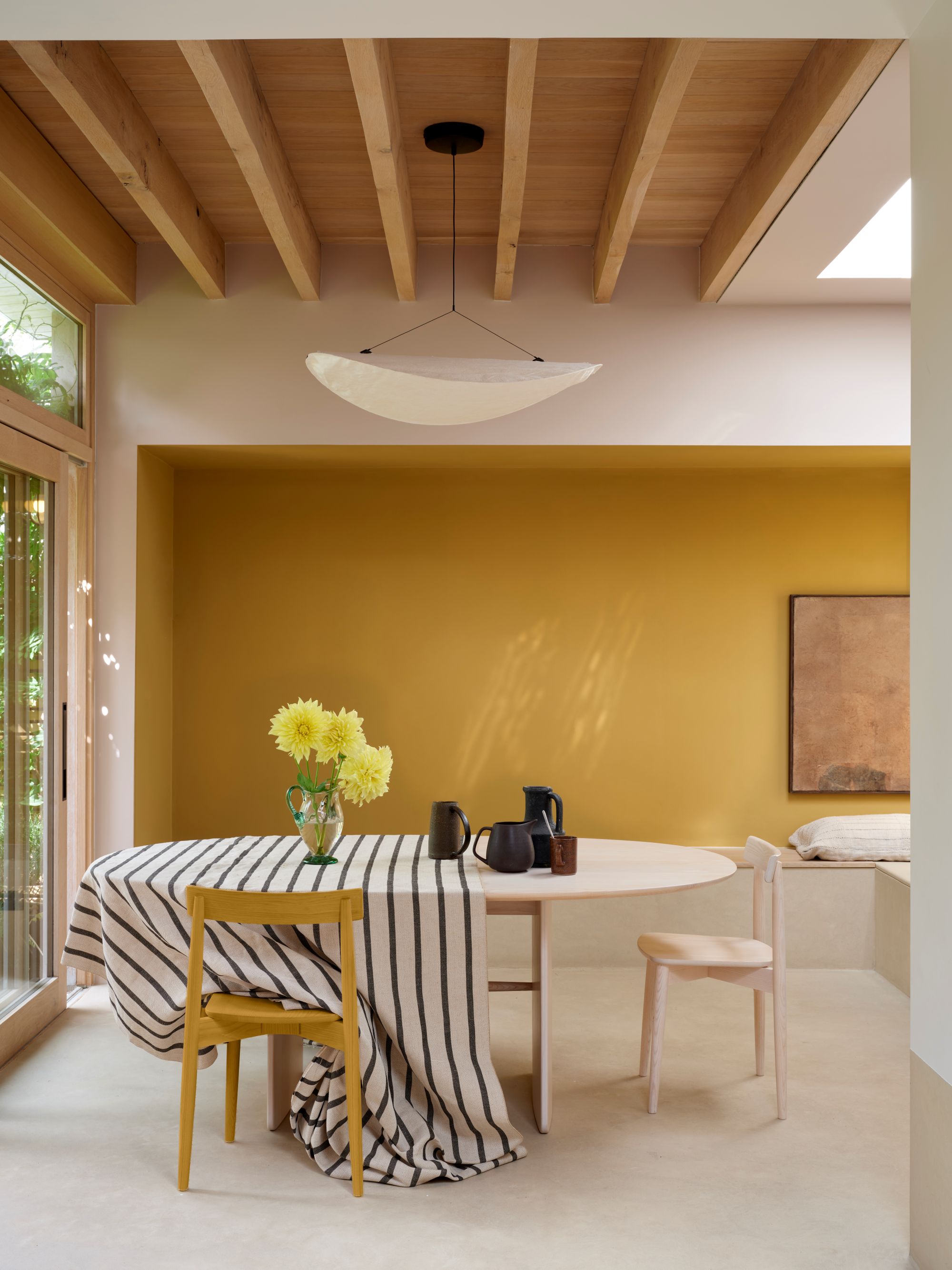 a yellow dining room with a light wood table and a striped tablecloth covering half of it