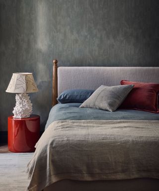 Dark gray bedroom with gray bed, gray bed linen, gray and red cushions, red side table, cream textured lamp