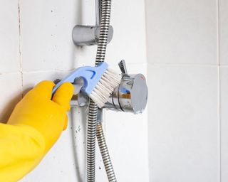 Person cleaning shower, scrubbing with a brush wearing rubber gloves