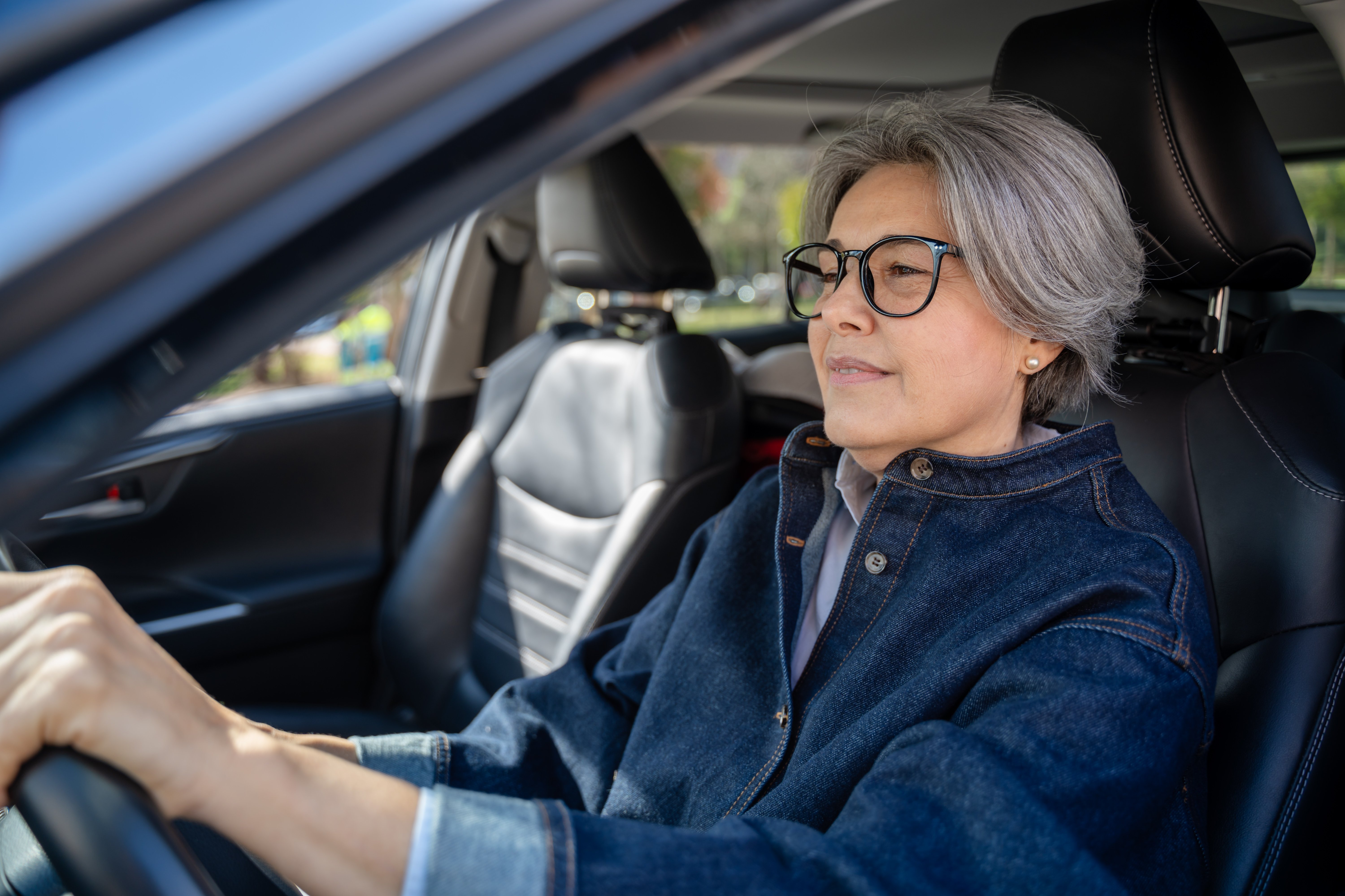 A senior woman with glasses is driving a car.