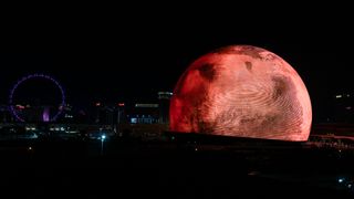 a giant spherical LED screen lit up to look like the moon, Mars and Earth