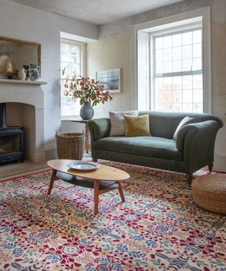 winter decor ideas, neutral living room with large patterned rug, green couch, plaster style walls, fireplace, vase of seasonal foliage, retro coffee table
