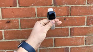 Fitbit Charge 5 held up against red brick wall