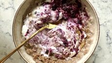 A bowl of porridge with yoghurt and jam swirled in, a brass-colored, shiny spoon rests in the bowl