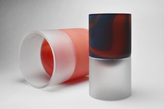 Two cylinder shaped glassed (one laying on its side and one upright) with half contemporary glass design and half frosted glass design, photographed against a grey background