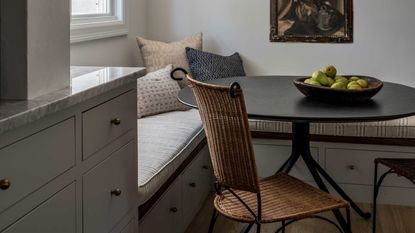 small dining nook with rattan chair, window seat, artwork, and bowl of pears