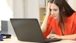 An annoyed looking woman sitting at a desk and using a laptop