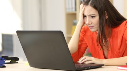 An annoyed looking woman sitting at a desk and using a laptop