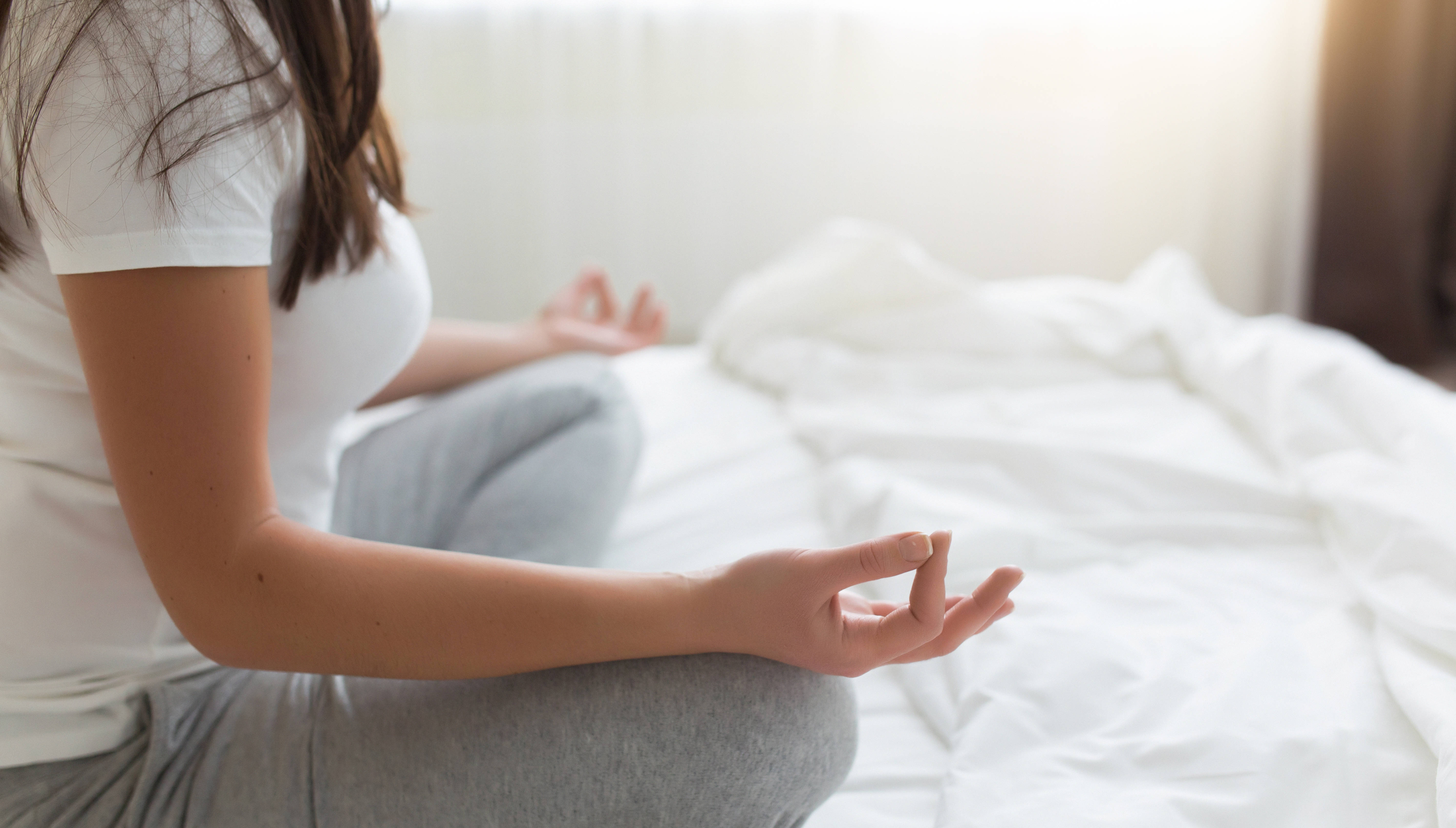 A woman meditates on her bed as part of her relaxing bedtime routine to ease back pain