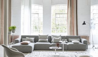 white living room with gray sectional, console, side tables, rug, stripe drapes
