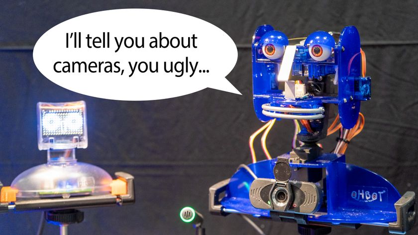 Talking Ohbot robots with speech bubble. One robot says "I'll tell you about cameras, you ugly..." to the other.