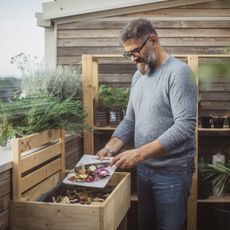 A man in glasses scrapes food scraps off a cutting board into a wooden compost bin