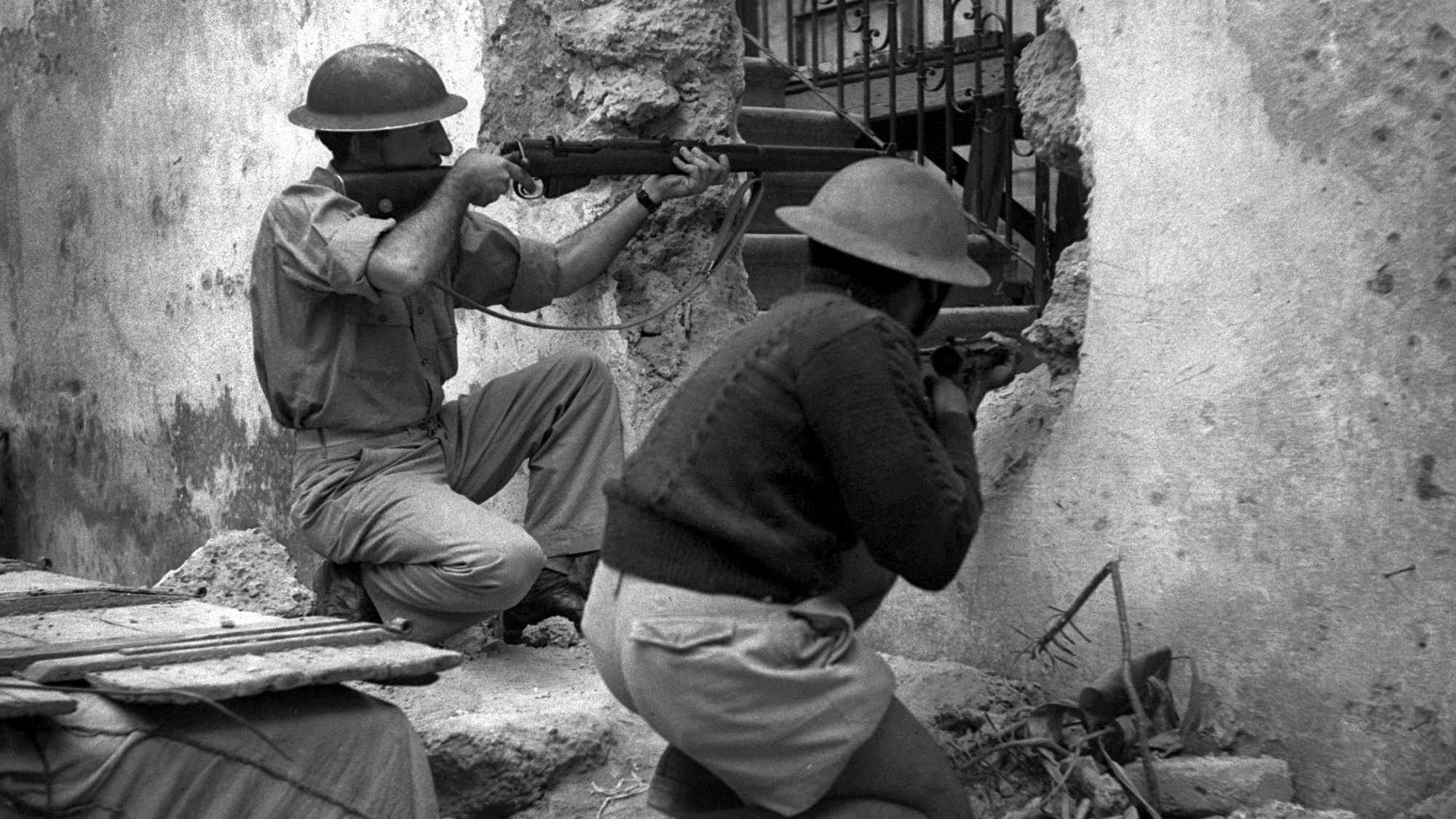 Haganah militia soldiers wearing helmets and armed with rifles engaged in a firefight