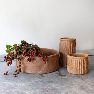 Three cement bowls sit atop a grey stone surface, the left-end side one filled with red berries.