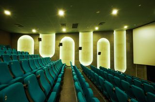 A cinema with green chairs and long thick rounded wall lights.