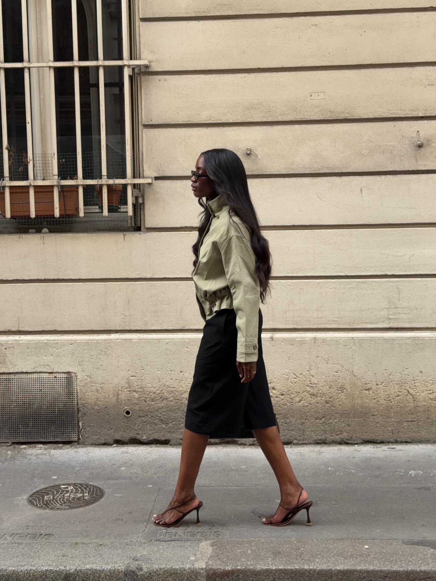 Liv wearing a funnel neck jacket, black skirt and strappy heeled sandals