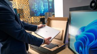 Dell laptop being removed from its box on a desk next to a monitor