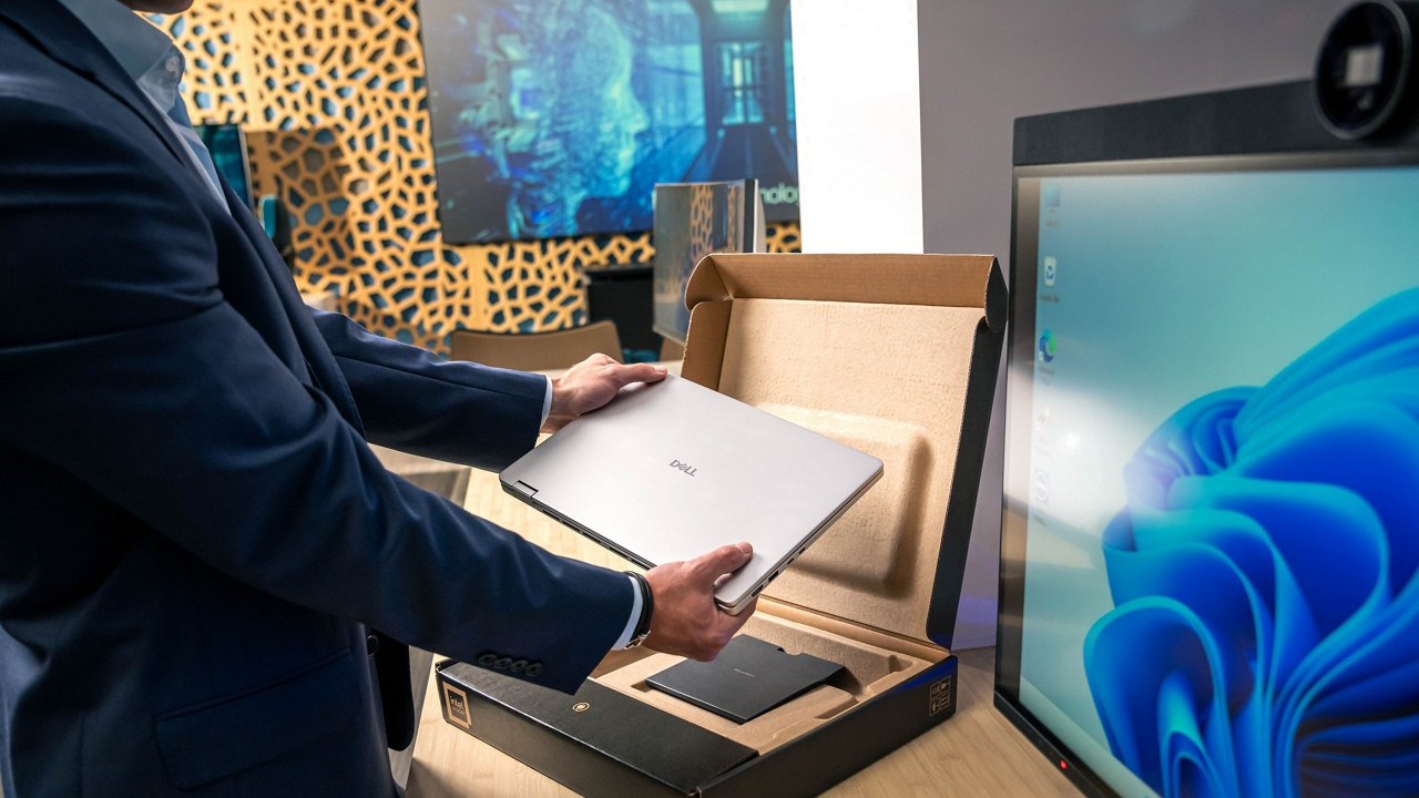 Dell laptop being removed from its box on a desk next to a monitor