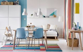 Colorful dining space with multi-stripe rug and drapes, and baby blue dining chairs.