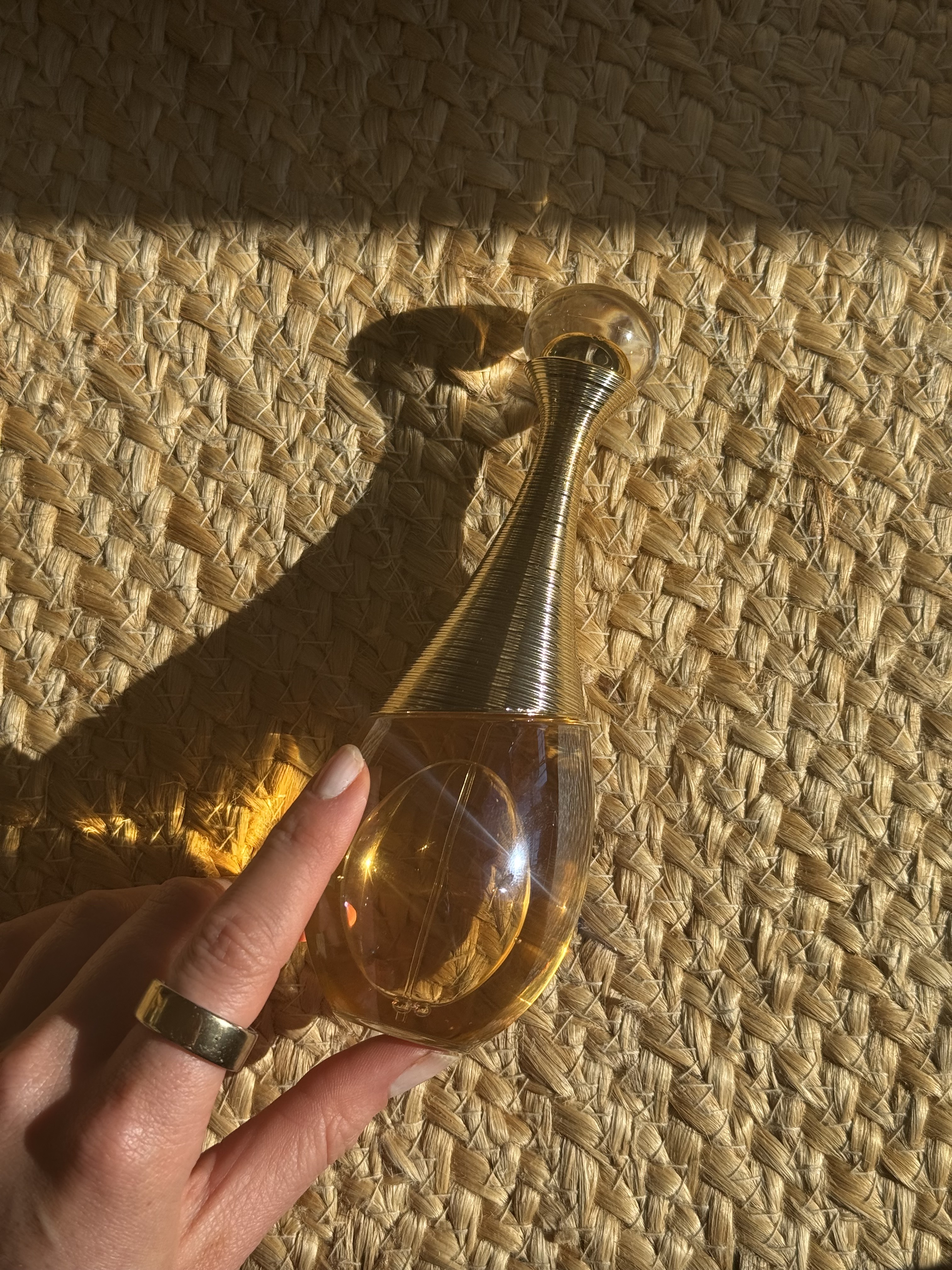 A bottle of Dior J'adore Intense parfum on a raffia textured background