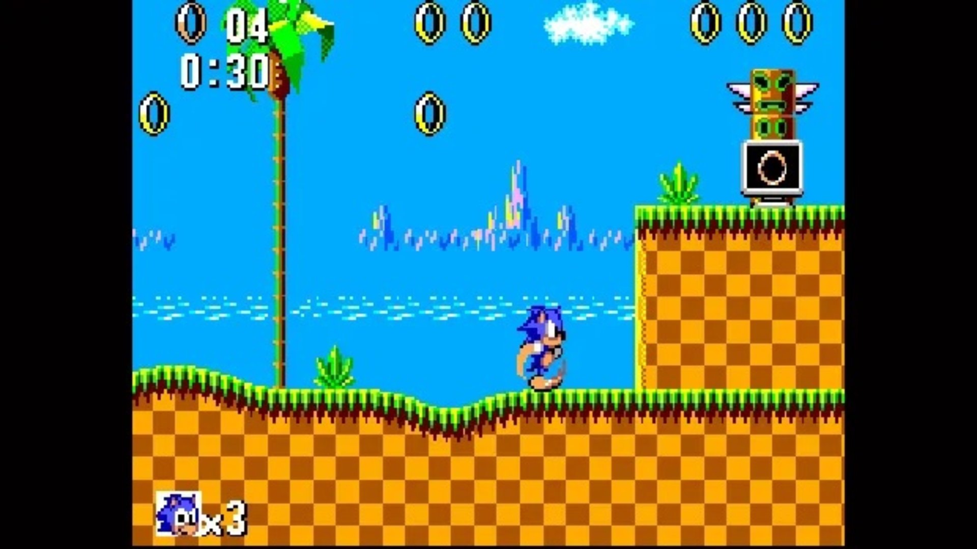 Sonic the Hedgehog screenshot of Sonic running across a grassy platform which has gold rings up in the air and another tier higher up with a gold ring on a tv screen