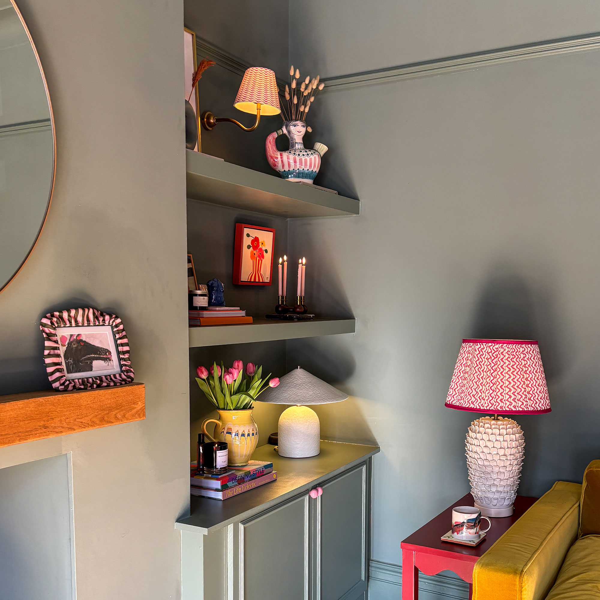 Corner of green living room with lamp on red side table, and another sample lamp on open built-in shelving