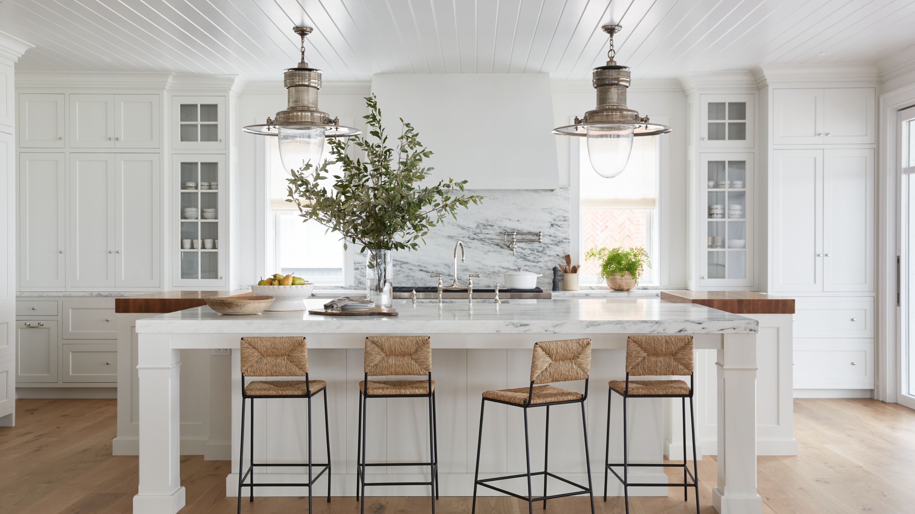 A sprawling marble island anchored by woven seagrass stools and statement industrial brass pendants, perfect for casual seaside entertaining.