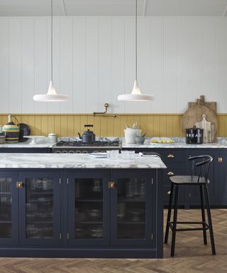 Panelled kitchen wall decor painted mustard yellow in a white scheme with midnight blue cabinetry.