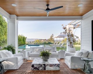 Living area with white sofa and two white armchairs open to backyard with pool