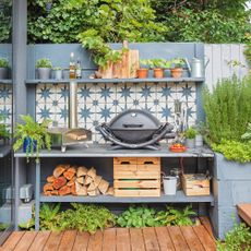 an outdoor kitchen on a patio with a bold tiled splashback and a Weber portable barbecue showing budget garden ideas