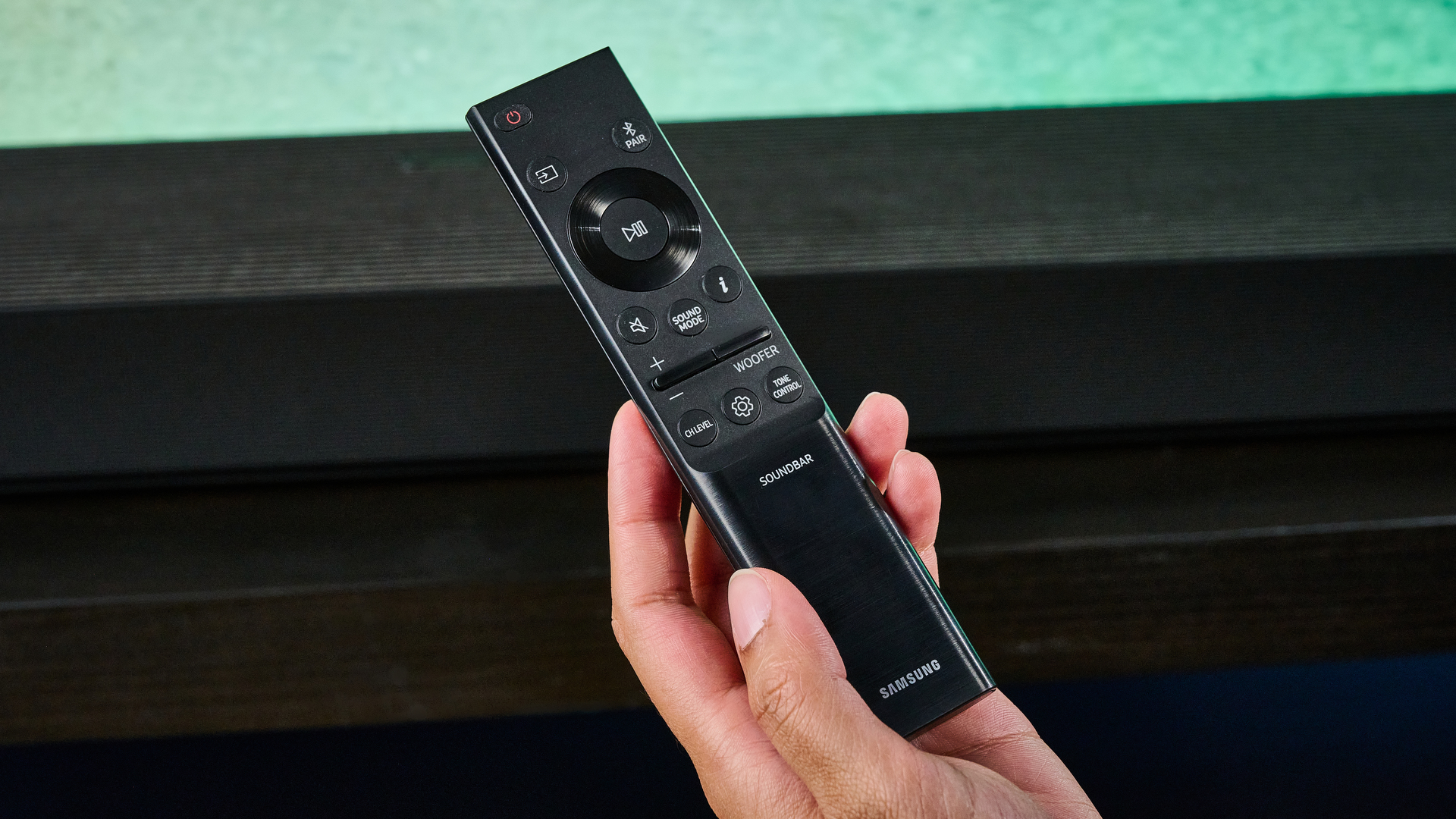 the samsung qs90h soundbar in a living room set with a tv and photographed with the blue tom's guide background